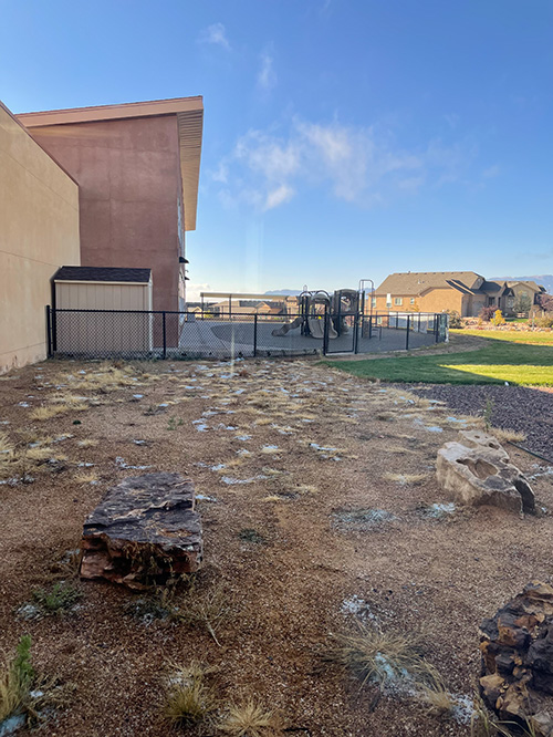 Photograph of dead grass and rocks in front of an elementary school playground.
