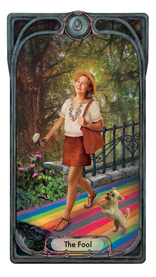 Tarot card The Fool shows a girl walking cheerfully along a rainbow path, her dog jumping at her feet