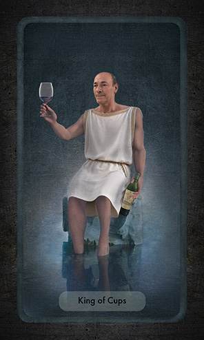 The King of Cups shows an older man seated on a rock, his feet and lower leg submersed in the pool that surrounds him. His right hand holds a glass of red wine raised in a toast, his left had loosely holds the bottle by his side.