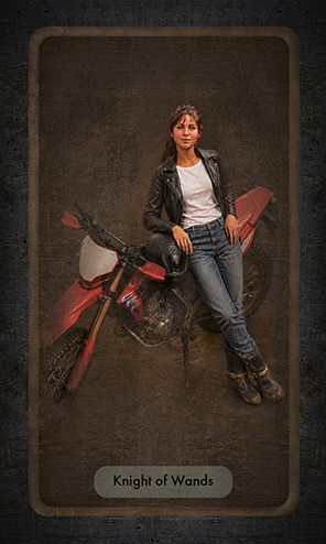The Knight of Wands shows a young woman in jeans and a black leather jacket leaning against a red adventure bike. She projects confidence and fearlessness.