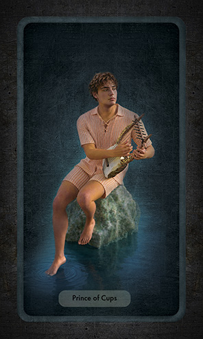 The Prince of Cups shows a handsome young man seated on a jade rock, his right foot dangling in the water that surrounds him, strumming dreamily on an ancient Greek lute. He is dressed in a pale orange striped top and shorts of linen.